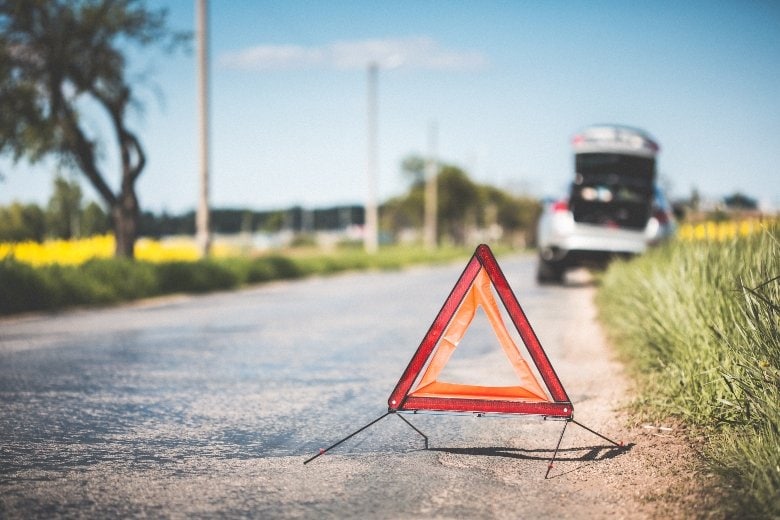 A traffic warning triangle placed behind a car on the roadside